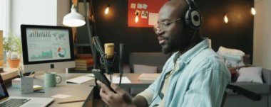 Tekerlekli sandalyede oturan, akıllı telefon ekranından mesaj okuyan ve ev stüdyosunda iş podcast 'i yaparken mikrofonla konuşan Afrikalı Amerikalı bir adam.