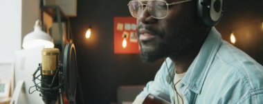 Evde kayıt stüdyosunda Afrika kökenli Amerikalı bir adamı gitar çalarken ve mikrofonda şarkı söylerken çek.