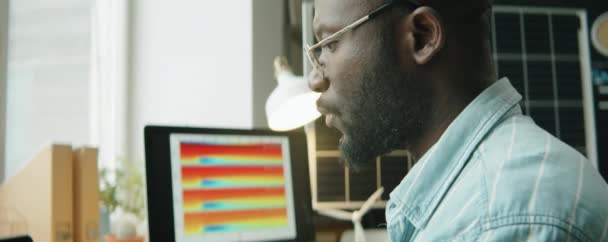 非洲裔美国人可持续能源工程师在写字台工作时使用笔记本电脑和用杯子喝咖啡的近照 — 图库视频影像