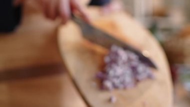 Rack focused tit down shot of hands of male cook putting chopped red onion from wooden cutting board into glass bowl