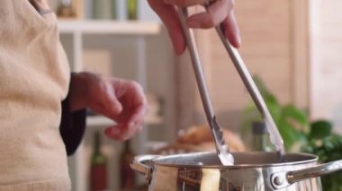 Erkek şefin çok renkli spagettiyi metal maşayla kaynayan sudan alıp tencerede makarna pişirirken görüntüsünü kapatın.