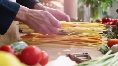 Makarna pişirmeye hazırlanırken erkek aşçının mutfak masasına rengarenk spagetti serdiği yakın plan.