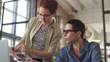 Ofiste birlikte çalışırken dizüstü bilgisayarla belge ve proje tartışan iki profesyonel iş kadını.