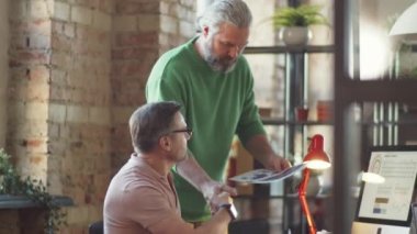 Olgun iş adamı, ofiste çalışan erkek arkadaşla belge ve projeyi bilgisayarda tartışıyor.