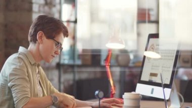 İş kadınının cam ofis duvarından bilgisayar kullanarak ve masa başında çalışırken bazı notlar yazarak görüntüle