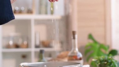 Erkek aşçının, mutfakta yemek pişirirken kaynar suya tuz kattığı seçici odak noktasını kapat.