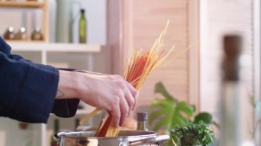 Erkek elinin, mutfakta makarna pişirirken kaynar suyla bir demet spagettiyi tencereye koyarkenki yakın çekimi.