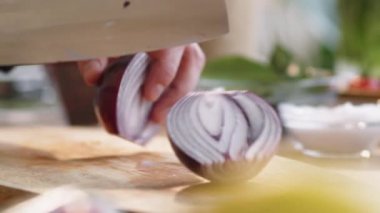 Erkek ellerinin kırmızı soğan ampulünü keserken ve yarısını kasap bıçağıyla keserken yakın plan çekimleri.