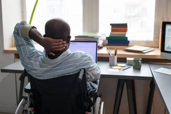 Человек, сидящий на инвалидной коляске и работающий на ноутбуке — стоковое фото