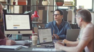 Orta yaşlı iş kadını, ofiste takım arkadaşlarıyla bilgisayar ekranında çizelgeleri tartışıyor.