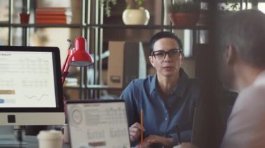 Orta yaşlı bayan takım lideri iş görüşmesinde iş arkadaşlarıyla bilgisayardaki grafikleri tartışırken aynı zamanda iş projesinde de birlikte çalışıyor.
