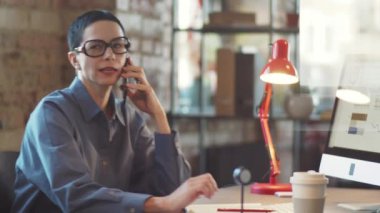 Masada otururken cep telefonuyla konuşan orta yaşlı iş kadınının cam ofis duvarından bak