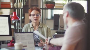 Yetişkin erkek meslektaşlarıyla ofiste yapılan takım toplantısında belgeyi tartışan kadın yönetici.