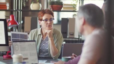 Ofis toplantısında meslektaşlarıyla proje üzerinde çalışırken bilgisayar ve kağıt üzerinde çizelgeleri tartışan bayan takım lideri
