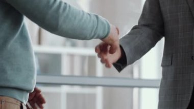 Resmi kıyafetli tanınmayan iki erkek meslektaşın el sıkışarak ve ofiste iş tartışarak birbirlerini selamladıkları orta bölüm çekimleri.