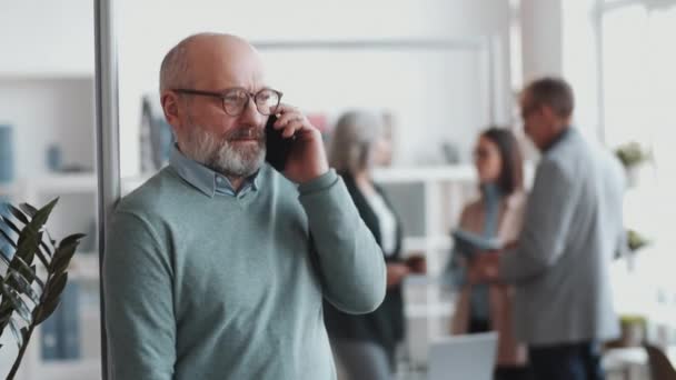 Vidám Idős Üzletember Támaszkodik Üveg Fal Irodában Mosolyog Beszél Mobiltelefon — Stock videók
