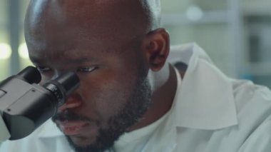 Bilimsel deney yaparken Afrikalı Amerikalı laboratuvar çalışanının mikroskoptan bakarken yakın plan fotoğrafı.