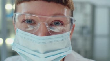 Koruyucu maske ve gözlüklü genç kadın laboratuvar bilim adamının yakın plan portresi.