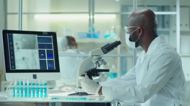 Científico Afroamericano Mascarilla Protectora Gafas Guantes Médicos Usando Microscopio Conectado — Vídeos de Stock