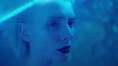 Gotik makyajlı ve siyah sclera lensli genç bir kadın stüdyoda duruyor.