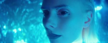 Kapalı kontak lensli ve yaratıcı makyajlı çekici genç bir kadının yakın plan portresi. Stüdyoda, yüzünde mavi neon ışığı ve lazer ışınları olan bir poz veriyor.