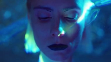 Stüdyoda lazer ışığı altında poz verirken kameraya bakan karanlık lens ve gotik makyajlı güzel bir kadının yaratıcı portresi.