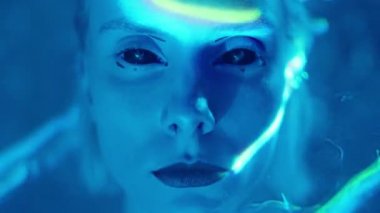 Kapalı kontak lensli ve uzaylı makyajlı genç bir kadının karanlık stüdyoda lazer ışığıyla dolu poz verirken yakın plan çekimleri.