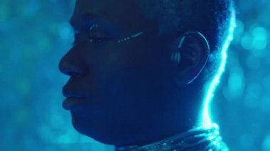 Stüdyoda mavi lazer ışığıyla dolu kabile makyajlı Afro-Amerikan bir adamın yan görüntüsü.