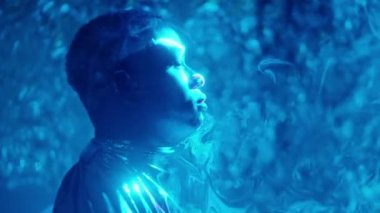 Parlak elbiseli Afro-Amerikan bir adamın, gökyüzü lazer ışığının düz tabakasında dikilirken yan görüntüsü.