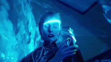 Koyu renk rujlu, karartma lensli, metalik cüppeli, stüdyoda kameraya poz veren uzaylı bir kadın.