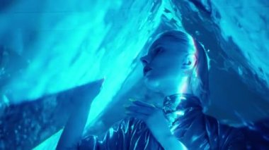 Koyu renk rujlu, neon tırnaklı ve kontak lensli çekici uzaylı kadın stüdyoda kameraya mavi lazer ışığı ile poz veriyor.