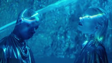 Yaratıcı makyajlı, siyah gözlü, parlak elbiseler giyen, stüdyoda sis ve mavi lazer ışığına bakan, hipnotize olmuş uzaylı kadın ve adam.