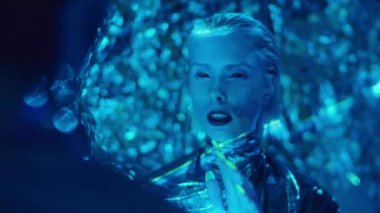 Omuzlarının üzerinden, siyah gözlü, parlak elbiseli, mavi lazer ışığıyla odada dikilen ve biriyle konuşan uzaylı bir kadının fotoğrafı.