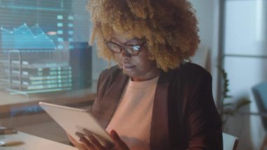 Afrikalı Amerikalı iş kadını geceleri yatırım şirketinde çalışırken dijital tabletle yazı yazıyor.