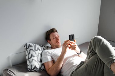 Beyaz tişörtlü, tatmin olmuş beyaz tenli genç adam sohbet ederek, sörf yaparak, bilgisayarla uğraşarak ve yatak odasının içindeki yatakta telefonla konuşarak uyandı. Uzak iletişim için modern aygıt, komik video