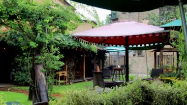 Şemsiyeli bahçe, bahçe süslerle dolu arka planda ise Val 'Quirico kasabasında yağmurlu bir günde tüten odunları ve dinlenmek için terası olan bir ısıtıcı görebilirsiniz.