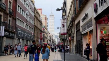 Mexico City, Meksika - Eylül 2021: Mexico City sokaklarında yürüyen insanlar, arka planda 15 Eylül anısına Meksika bayrağını gösteren Latin Amerika kulesini görebilirsiniz..