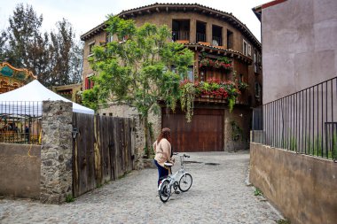 Tlaxcala, Mexico - June 2021: Girl walking with her bicycle in the town Val'Quirico while a light drizzle falls, a place where you can see European influence in the architecture. clipart