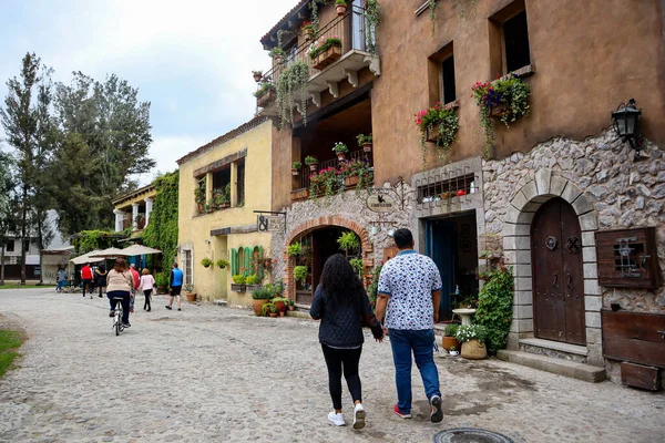 Tlaxcala, Meksika - Haziran 2021: Val 'Quirico caddelerinde yürüyen bir çift, hediyelik eşya dükkanları olan evler ve binaların yanında, sokaklar çiçek ve bitkilerle süslenmiş..