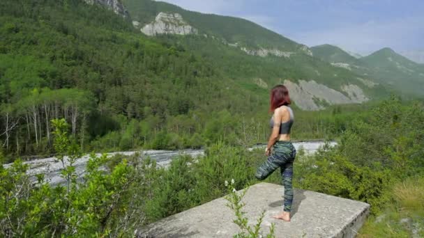 女性は山の中の川の近くでヨガをやってフィット — ストック動画