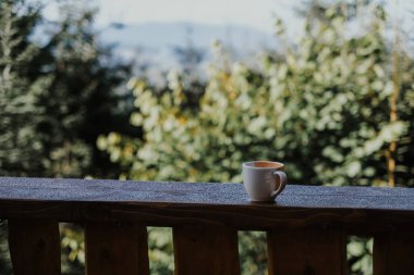 Ahşap bir çitin üzerinde duran el yapımı bir bardak. Gün batımında arka planda dağ manzaralı ahşap bir çitin üzerinde duran el yapımı bir bardakla güzel bir sahne. Karpatlar, Ukrayna.