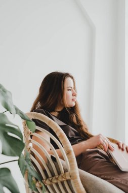 Yeşil bitkinin etrafında saman bir sandalyede oturan güzel kız başka tarafa bakıyor ve düşünüyor. Çeşitli duygu ve ruh halleriyle farklı tarzlarda bir kızın stüdyo portreleri..