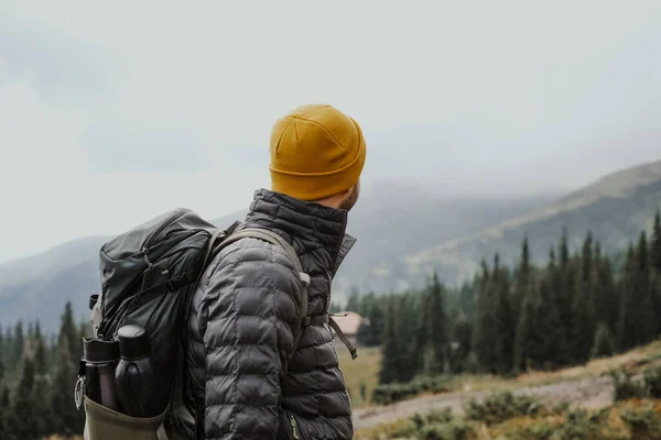 Man with backpack looking at mountains. Hiker in yellow beanie with backpack watching clouds over the Carpathians in Ukraine.