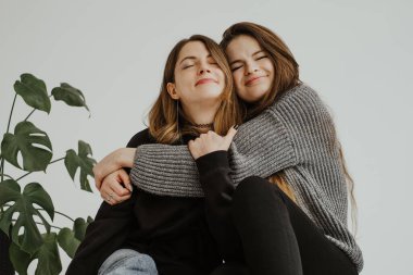 İki genç kadının sarılıp mutlu olduğu bir stüdyo fotoğrafı. Yan yana oturan iki kadının portreleri. Yanında bir canavar bitkisi, sarılıyor, duygularını ve duygularını ifade ediyor..