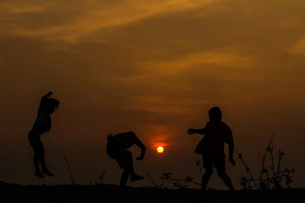 Silueta, grupo de niños felices jugando en el prado, puesta del sol, s — Foto de Stock