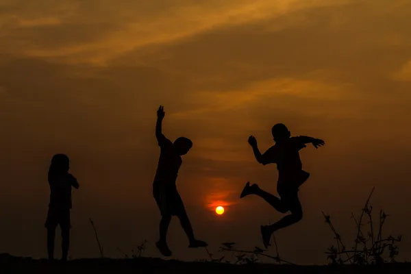 Silhouette, Gruppe fröhlicher Kinder, die auf der Wiese spielen, Sonnenuntergang, Stockfoto