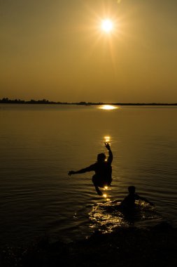 gün batımında göle atlamayın siluetleri bir adam.
