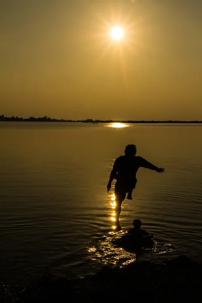 Silhouettes of man who jump off into lake at sunset. — Stock Photo, Image