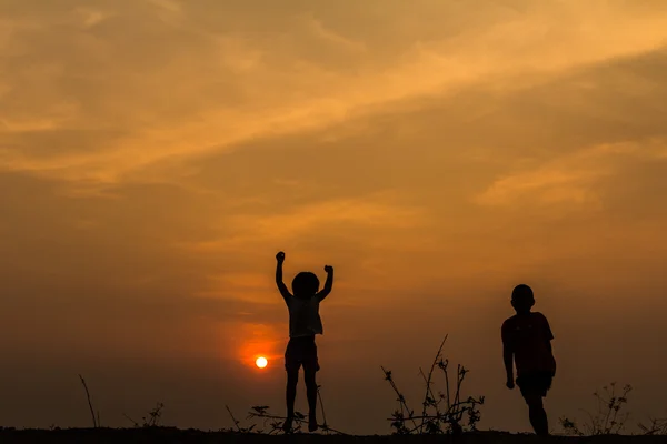 Silhouette, Gruppe fröhlicher Kinder, die auf der Wiese spielen, Sonnenuntergang, Stockbild
