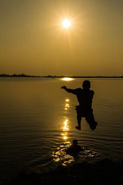 Silhouettes de l'homme qui saute dans le lac au coucher du soleil . Photo De Stock